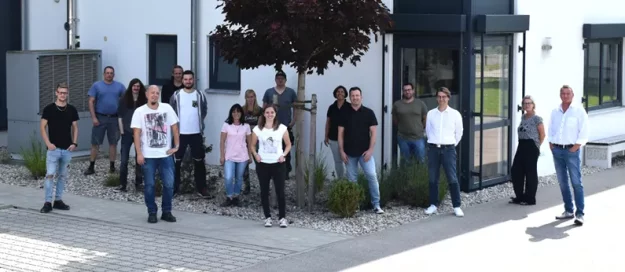 rolf weigel Jubiläum mit einem Gruppenbild der Mitarbeiter vor dem Gebäude