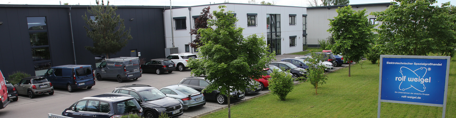 Ein Gebäude mit einem Parkplatz, einer Grünfläche und einem Schild der Firma rolf weigel