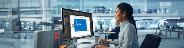 Eine Frau arbeitet in einem Großraumbüro an einem PC. Auf dem Bildschirm sieht man den Cembre EPlan.