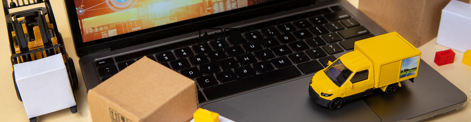 Ein Laptop, auf dem ein kleiner gelber Lieferwagen und neben dem eine kleiner Gabelstapler stehen, die als Symbol für Logistik und Kommissionierung stehen