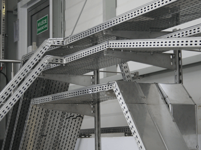 Mehrere übereinander angeordnete Kabeltrassen aus Metall in einer industriellen Umgebung.