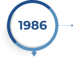 In einem weiße Kreis mit blauem Rahmen steht die Jahreszahl 1986 zur Symbolisierung der Unternehmensgründung in der Historie.